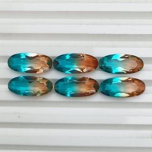 Op de afbeelding: Zes ovale edelstenen met een kleurovergang van turquoise naar amber. Elke edelsteen heeft een gefacetteerd oppervlak, dat het licht vangt en een sprankelend effect creëert. De edelstenen zijn gerangschikt in twee rijen van drie, wat hun gepolijste uiterlijk benadrukt.