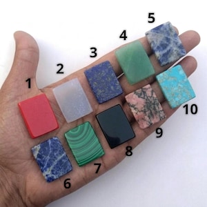 Puede incluir: Diez piedras preciosas pulidas rectangulares numeradas del uno al diez. Las piedras incluyen una piedra roja, una piedra blanca translúcida, una piedra azul oscuro con motas doradas, una piedra verde claro, una piedra azul y blanca, una piedra azul oscuro y blanca, una piedra verde con bandas, una piedra negra sólida, una piedra rosa y negra, y una piedra turquesa.