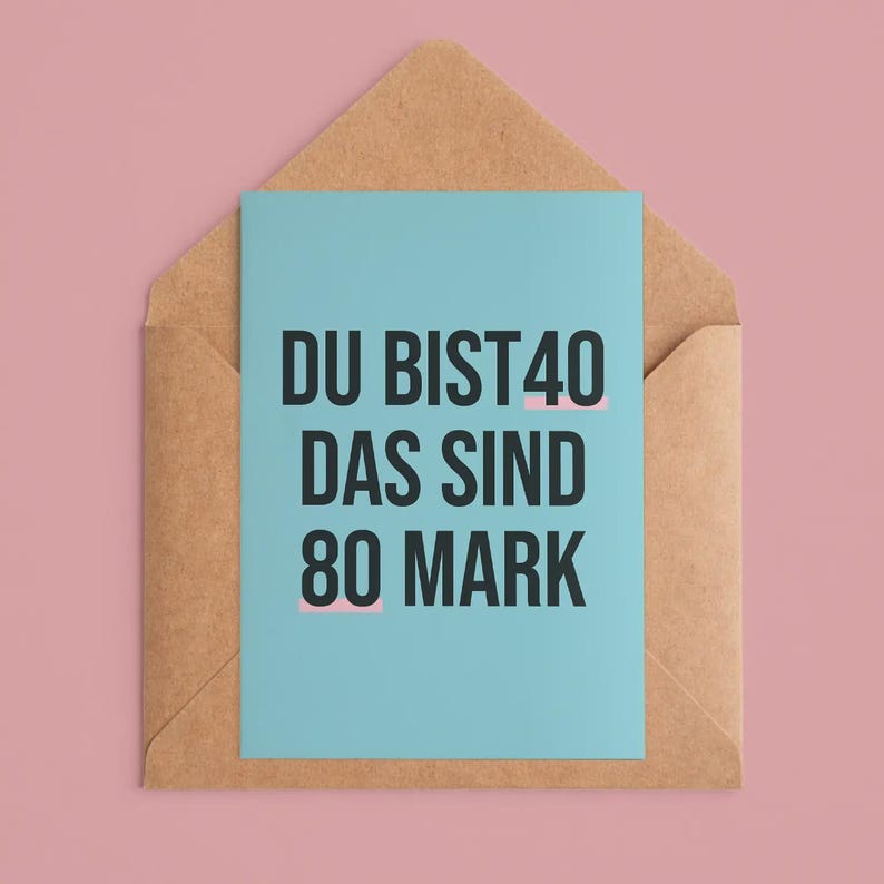 May include: A greeting card with the text "DU BIST 40 DAS SIND 80 MARK" in black font on a light blue background. The card is inside a brown envelope, set against a pink background.
