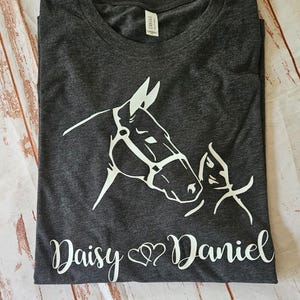 May include: A dark gray t-shirt with a white silhouette of a horse and a foal. The text "Daisy ♥ Daniel" is printed below the image.