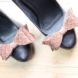 May include: A pair of black high-heeled shoes with brown leather bow accents. The bows have a woven pattern.