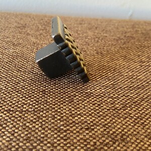 K&ouml;nnte beinhalten: Ein schwarzer Metall-Schrankknauf mit quadratischer Vorderseite und einem strukturierten Design.