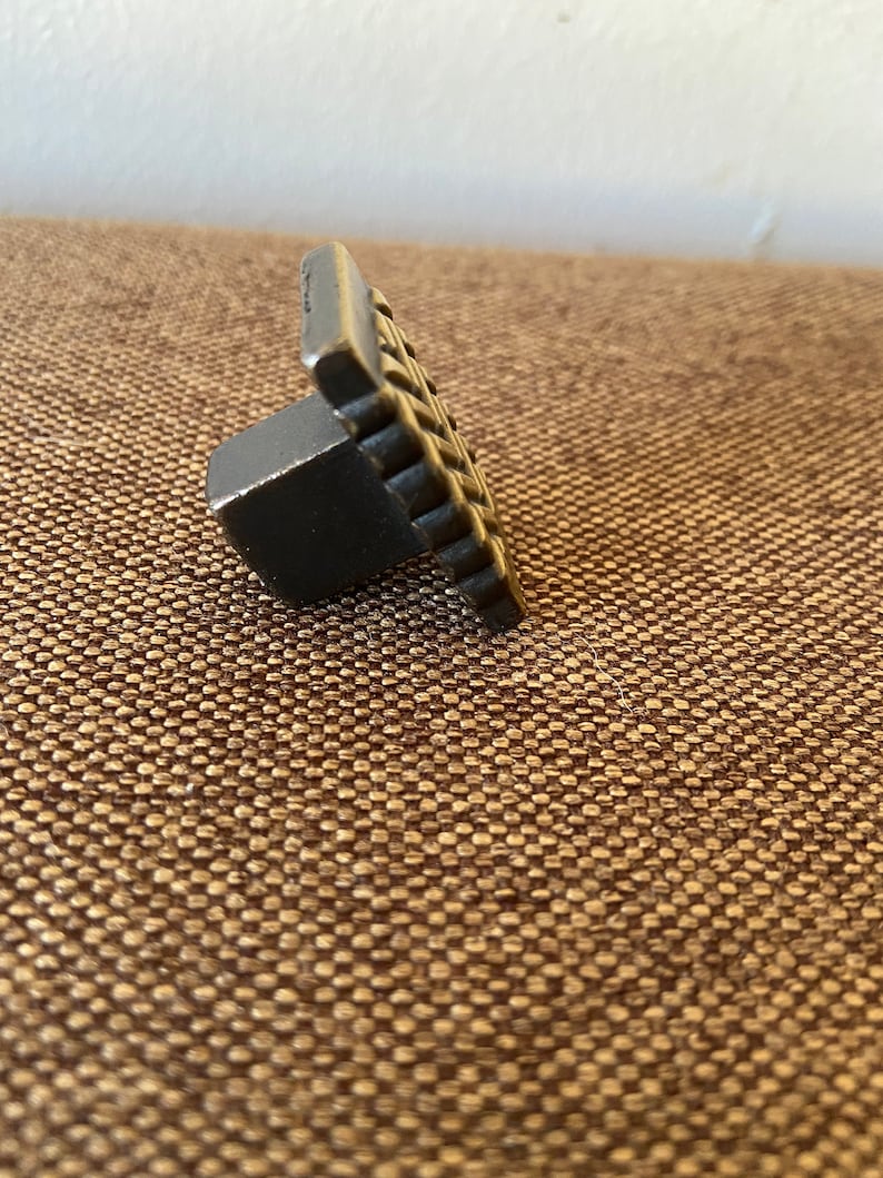 K&ouml;nnte beinhalten: Ein schwarzer Metall-Schrankknauf mit quadratischer Vorderseite und einem strukturierten Design.