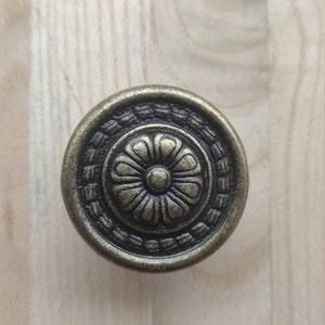 Peut inclure: Un bouton de porte rond en or antique avec un motif floral noir.