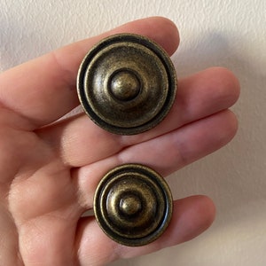 Może przedstawiać: Dwa okrągłe, antyczne złote gałki do szafek z wypukłym środkiem i koncentrycznymi okręgami.