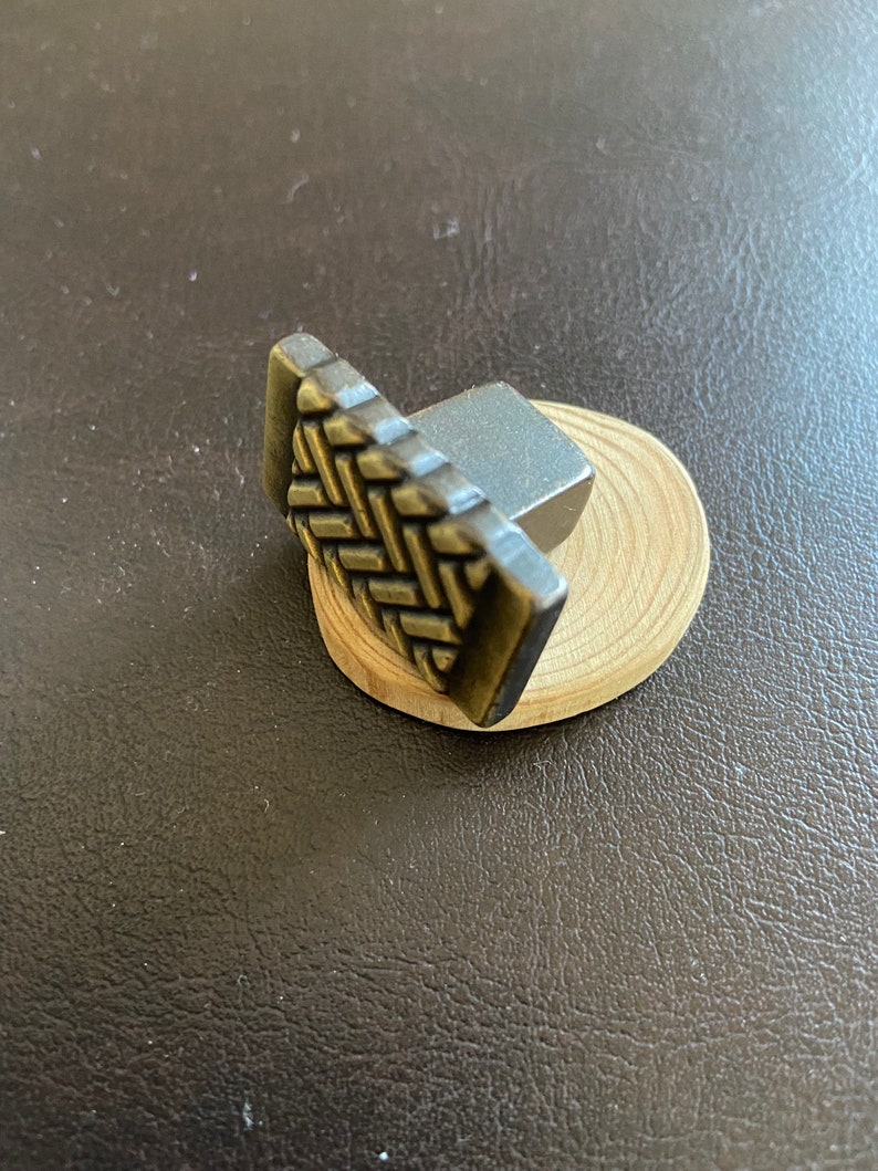 K&ouml;nnte beinhalten: Ein kleiner, dekorativer Metall-Schrankknauf mit einem gewebten Muster und einer silbernen Oberfl&auml;che. Der Knauf ist auf einem kleinen Holzsockel montiert.