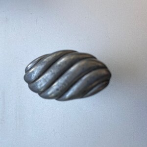 May include: A silver-toned, oval-shaped cabinet knob with a textured, twisted rope design. The hardware has a matte finish and is suitable for drawers or cabinet doors. The knob is approximately 3 inches long.