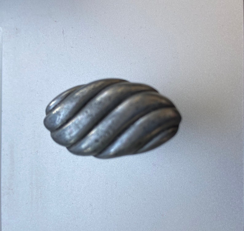 May include: A silver-toned, oval-shaped cabinet knob with a textured, twisted rope design. The hardware has a matte finish and is suitable for drawers or cabinet doors. The knob is approximately 3 inches long.
