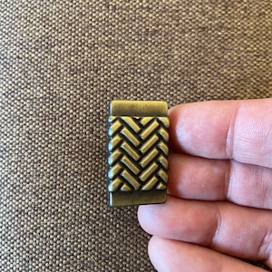 Peut inclure: Une petite poignée de tiroir rectangulaire de couleur laiton avec un motif tissé.