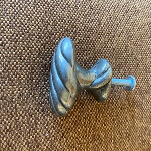 May include: A silver-colored cabinet knob with a decorative, twisted design. The knob is attached to a screw with a blue head. The hardware is likely for a drawer or cabinet.