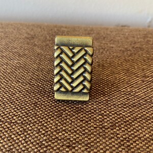 K&ouml;nnte beinhalten: Ein goldfarbener Metall-Schrankknauf mit gewebtem Design.