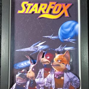 Könnte beinhalten: Eine gerahmte 3D-Illustration der Star Fox-Videospielfiguren. Die Figuren sind Fox McCloud, Falco Lombardi, Peppy Hare und Slippy Toad. Der Hintergrund ist eine dunkelblaue Weltraumszene mit Sternen und Planeten.