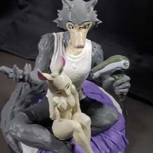 Puede incluir: Figura detallada que representa dos personajes antropomórficos. Uno es una figura gris con forma de lobo que lleva una camiseta sin mangas blanca y detalles morados. El otro es una figura blanca con forma de conejo. El lobo sostiene un objeto verde. La base es negra.