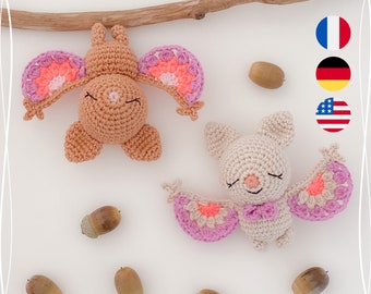 May include: Two crocheted bats with pink and orange wings. The bat on the left is brown and the bat on the right is white.