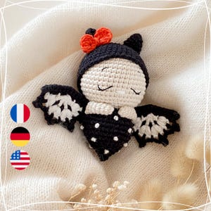 Könnte beinhalten: Ein gehäkeltes Fledermausspielzeug mit schwarz-weißen Polka-Dot-Flügeln, einem schwarzen Hut und einer roten Schleife. Das Spielzeug hat ein weißes Gesicht mit schwarzen Augen und einem aufgestickten Schnurrbart.