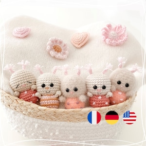May include: Five crocheted ladybug toys in a wicker basket. The ladybugs are pink and white with black eyes and are arranged in a row. The basket is on a white knitted surface.