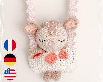 May include: A crocheted pink and white deer toy with closed eyes hanging from a pink crocheted strap. The deer is wearing a pink and white crocheted dress with a heart-shaped design.