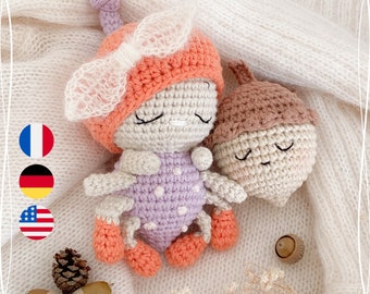 May include: Two crocheted amigurumi toys, a purple and orange ladybug and a brown acorn, are lying on a white fuzzy surface. The ladybug has a white bow and closed eyes. The acorn has a closed mouth and closed eyes.