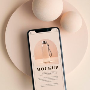 Puede incluir: Una maqueta de teléfono inteligente negro con un fondo blanco que muestra una botella de agua de vidrio transparente con una correa gris. El texto "MOCKUP" y "Place Your Design Here" se muestra en la pantalla.