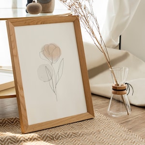 Peut inclure: Une impression encadrée d'un dessin minimaliste d'une fleur sur fond brun clair. L'impression est dans un cadre en bois clair et repose sur une table avec un vase de fleurs séchées.