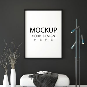May include: A black and white photo frame mockup with the text "MOCKUP YOUR DESIGN HERE" on a black wall. A white ottoman with a grey throw blanket and a book on top sits in front of the frame. A black floor lamp with three blue lights is on the right side of the frame.