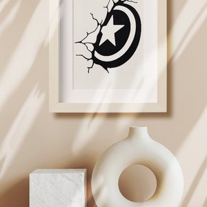 May include: A framed black and white illustration of a star inside a circle, breaking through a cracked wall. The illustration is displayed on a white shelf with a white ceramic vase with a circular opening.