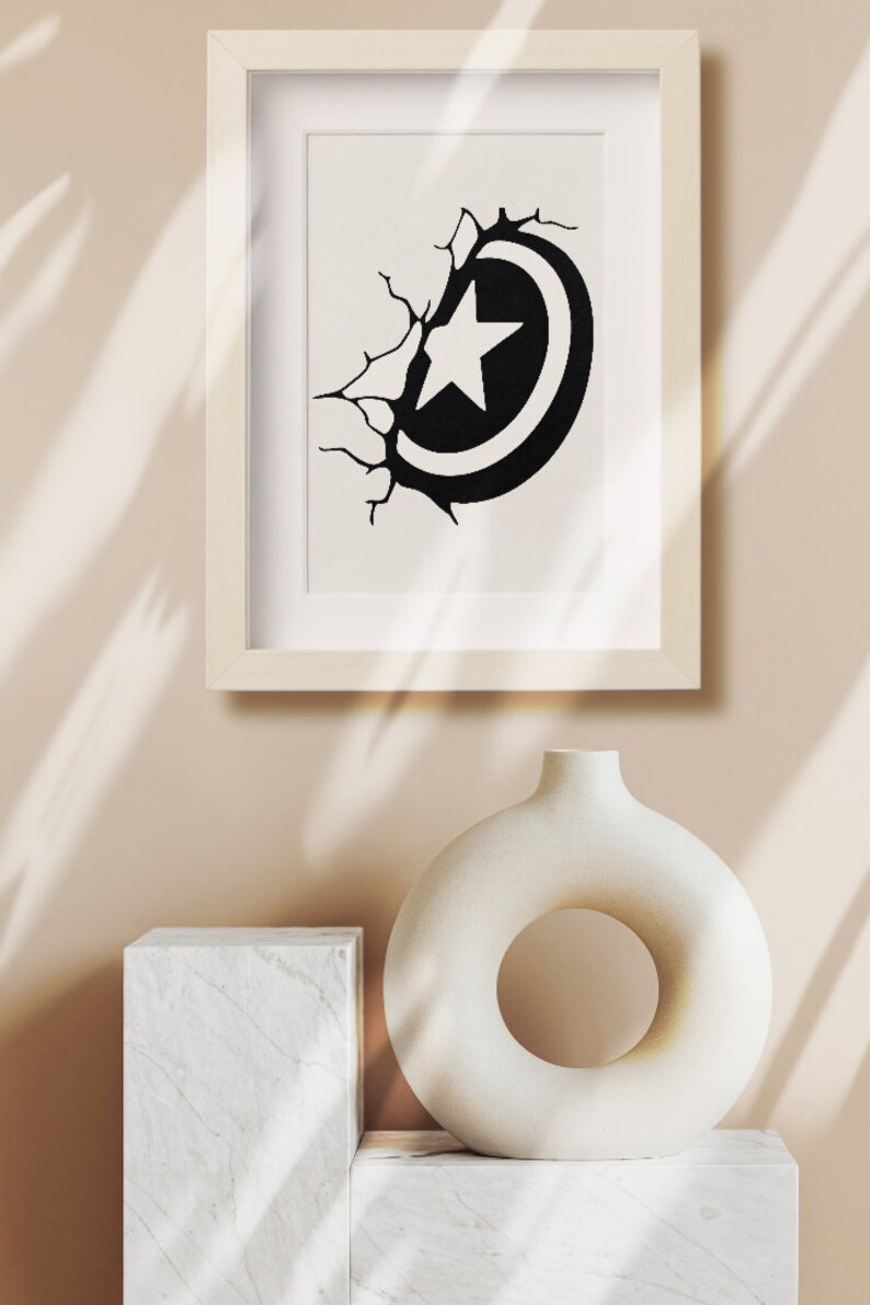 May include: A framed black and white illustration of a star inside a circle, breaking through a cracked wall. The illustration is displayed on a white shelf with a white ceramic vase with a circular opening.