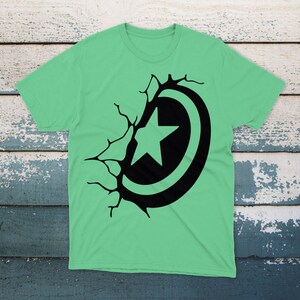 May include: A green t-shirt with a black graphic of a star inside a circle, breaking through a cracked wall.