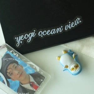 May include: A white plastic card with the text "yeogi ocean view" printed in blue. The card is on top of a black surface. A clear plastic card with a photo of a person wearing a hat and a blue and white graphic is on a white surface. A blue and white penguin figurine is on the white surface.