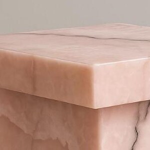 K&ouml;nnte beinhalten: Ein quadratischer, rosa Marmor-Beistelltisch mit einem soliden, blockartigen Sockel. Der Tisch hat eine glatte, polierte Oberfl&auml;che mit subtilen Maserungen. Das Gesamtdesign ist minimalistisch und modern, passend f&uuml;r verschiedene Einrichtungsstile.
