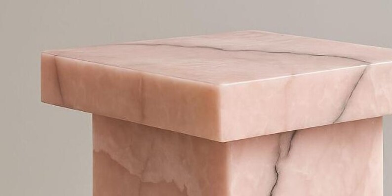 K&ouml;nnte beinhalten: Ein quadratischer, rosa Marmor-Beistelltisch mit einem soliden, blockartigen Sockel. Der Tisch hat eine glatte, polierte Oberfl&auml;che mit subtilen Maserungen. Das Gesamtdesign ist minimalistisch und modern, passend f&uuml;r verschiedene Einrichtungsstile.