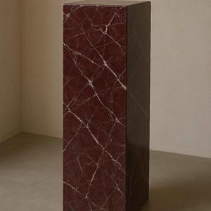 May include: A tall, rectangular pedestal with a burgundy marble-like finish. White veining creates a striking pattern across the surface. The minimalist design makes it suitable for displaying art or decor.