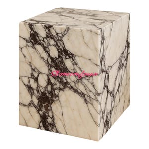 May include: A square marble block with a white and dark brown veined pattern. The block is a cube shape and appears to be a decorative item or small table. The marble has a polished finish.