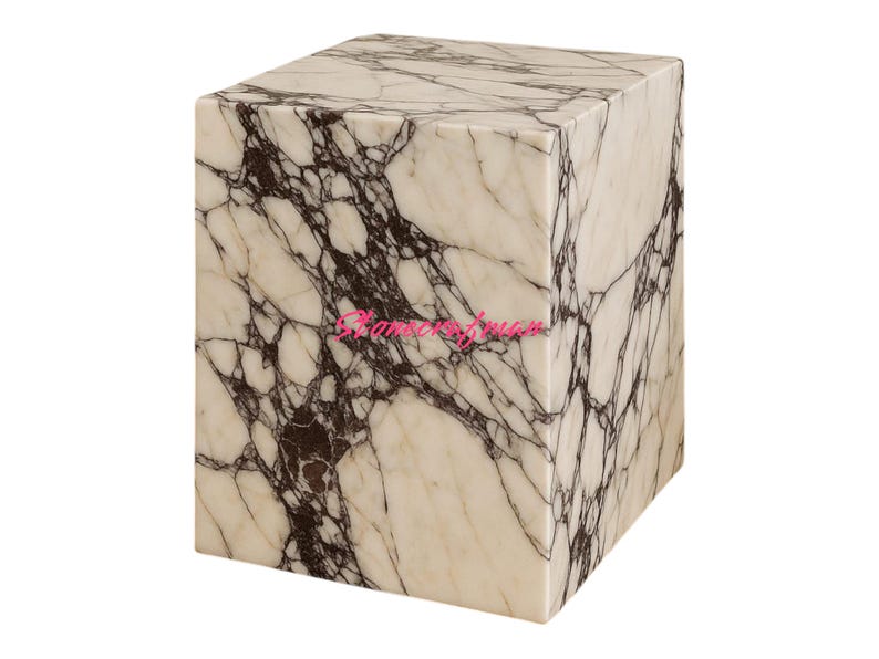 May include: A square marble block with a white and dark brown veined pattern. The block is a cube shape and appears to be a decorative item or small table. The marble has a polished finish.