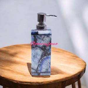 May include: Blue and white agate soap dispenser with a silver pump. The dispenser is sitting on a wooden table.
