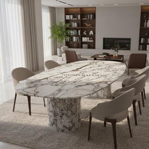 May include: An oval marble dining table with a white and gray veined pattern, supported by a cylindrical base. The table is surrounded by eight beige upholstered chairs with dark wooden legs. The text "STONECRAFTMAN" is visible on the table.