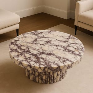 May include: A round coffee table with a marble top featuring a white and purple veined pattern. The base is cylindrical with vertical, rounded supports. The table sits on a light-colored rug, with neutral-toned furniture in the background.