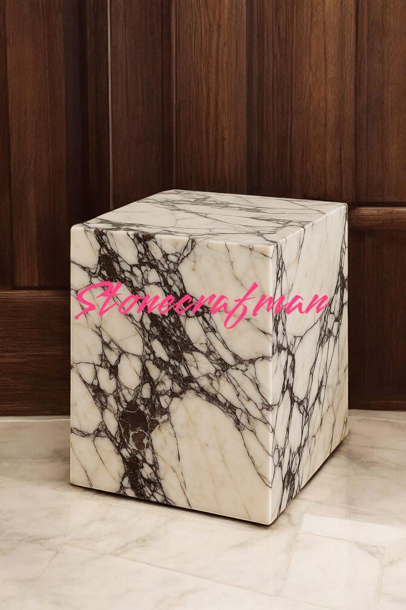 May include: A square marble side table with a white and dark brown veined pattern. The table is a cube shape and sits on a marble floor. The background is a dark wood panel.