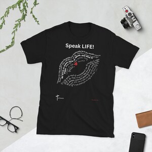 May include: Black t-shirt with a white graphic design of a heart with the words "Speak LIFE!" and a circular design of bible verses around the heart. The words "Be quick to listen, slow to speak, and slow to anger" are highlighted in red.