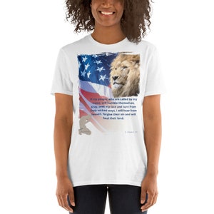 Könnte beinhalten: Weißes T-Shirt mit einem Löwen und einem amerikanischen Flaggen-Design. Der Text auf dem T-Shirt lautet: "Wenn mein Volk, das in meinem Namen gerufen wird, sich demütigt, betet, mein Angesicht sucht und sich von seinen bösen Wegen abwendet, werde ich vom Himmel hören, ihre Sünde vergeben und ihr Land heilen."