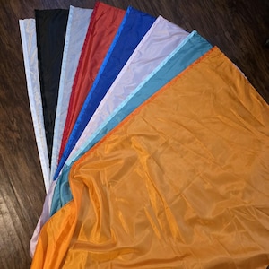 May include: A collection of colorful flags, fanned out to display their vibrant hues. The flags include shades of white, black, grey, red, blue, light blue, and orange. The flags are made of a shiny, lightweight material.