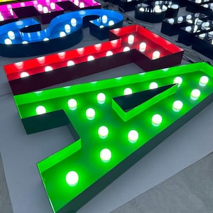 May include: A set of colourful, illuminated letters spelling out the word "ASIA". Each letter is made of metal and has a border of a different colour. The letters are lit with white LED lights.