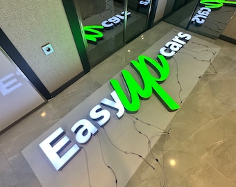 May include: A white and green 3D sign that reads "Easy Up Cars" is on a white surface. The sign is lit up with white lights and has wires running from it.