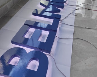 May include: Blue illuminated 3D letters spelling out "BELMONT" on a white surface. The letters are lit from within, creating a glowing effect.
