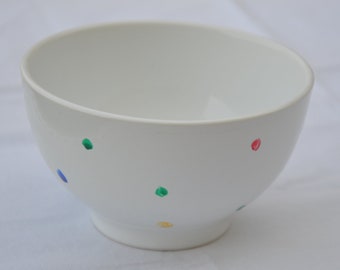 May include: A white ceramic bowl with a rounded shape and a small foot. The bowl is decorated with colorful polka dots in blue, green, red, and yellow. The bowl is likely for serving food.