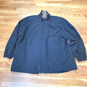 Puede incluir: Una chaqueta azul marino con cremallera, cuello alto y mangas largas con puños elásticos. El forro interior y el interior del cuello presentan un estampado de leopardo en blanco y negro, visible en los bordes y en la línea del cuello.