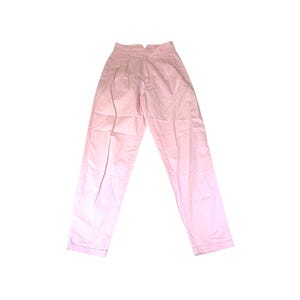 Puede incluir: Pantalones rosa claro de cintura alta con pliegues. Los pantalones tienen un diseño de pierna recta y están hechos de una tela ligera. Los pantalones están colocados sobre un fondo blanco.