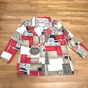 Könnte beinhalten: Ein langärmeliger Blazer mit einem geometrischen und verzierten Muster in den Farben Rot, Beige, Schwarz und Weiß. Das Kleidungsstück verfügt über ein steigendes Revers, einen Knopfverschluss auf der Vorderseite und eine strukturierte Silhouette mit kreisförmigen Motiven.