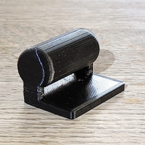 Könnte beinhalten: Ein schwarzes 3D-gedrucktes Objekt mit einer zylindrischen Oberseite und einer quadratischen Basis.