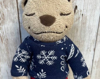 Può includere: Un orso di peluche marrone che indossa una camicia blu a maniche lunghe con un motivo a fiocco di neve bianco e pantaloni a quadri rossi e neri.